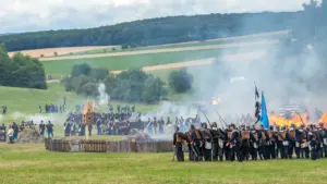 Historische Nachstellung einer Schlacht mit rauchender Infanterie und brennendem Dorf auf dem Feld.
