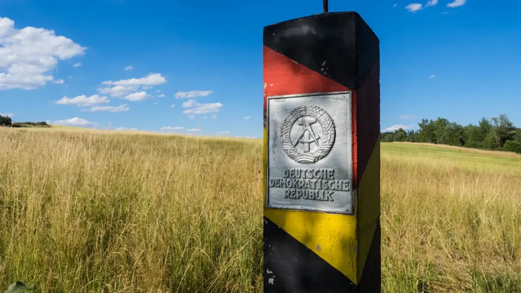 Historischer Grenzpfahl der ehemaligen DDR in einer ländlichen Umgebung bei blauem Himmel.
