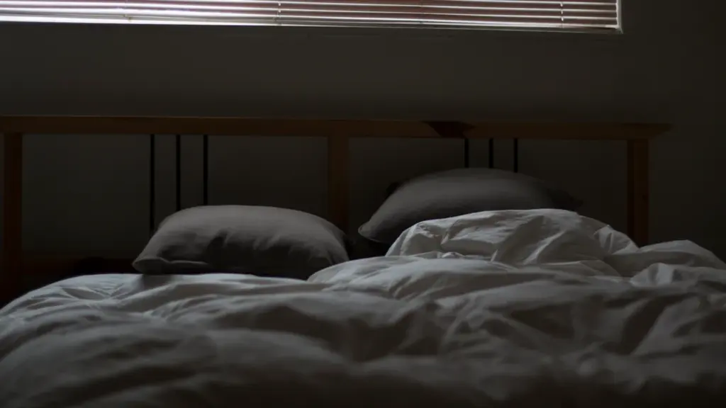 Ein ungemachtes Bett mit geschlossenen Jalousien bei abgedunkeltem Raum für besseren Schlaf.