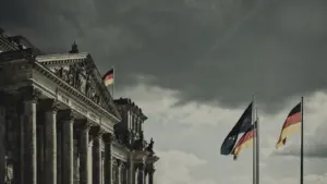 Das Deutsche Reichstagsgebäude unter einem dramatischen, bewölkten Himmel mit wehenden Flaggen.