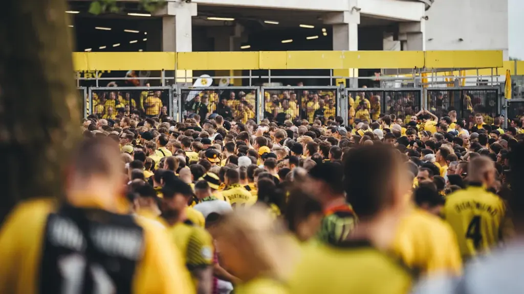 Viele Fans in gelben Trikots warten vor einem Fußballstadion auf den Einlass.