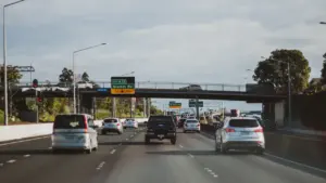 Autoverkehr auf einer Autobahn unter einer Brücke mit Straßenschildern bei Tageslicht.