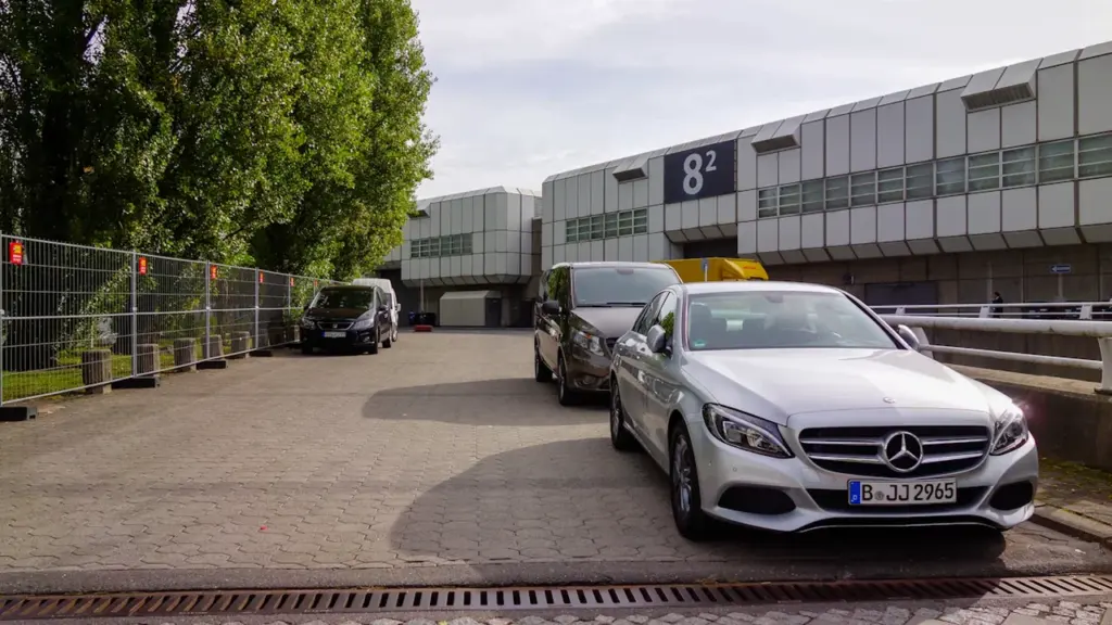 Parkende Autos vor einem Messehallengebäude am Berliner Messegelände unter bewölktem Himmel.