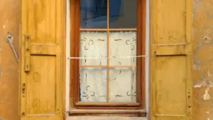 Offenes Holzfenster mit Fensterläden an einer alten Hausfassade bei sommerlicher Hitze.