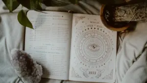 Ein aufgeschlagenes Notizbuch mit astrologischen Illustrationen neben einem Kristall und einer Pflanze.