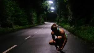 Eine Läuferin bindet sich nachts auf einer dunklen Straße die Laufschuhe zu.