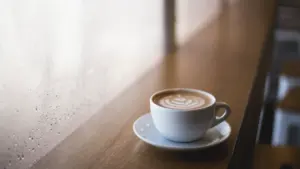 Eine Tasse Kaffee auf einem Holztisch neben einem Fenster an einem regnerischen Tag.