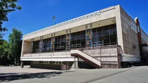 Modernes Gebäude mit großen Glasfenstern und bunten Glaselementen bei klarem blauen Himmel.