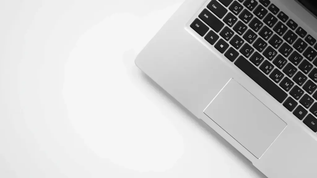 Nahaufnahme einer silbernen Laptop-Tastatur mit lateinischen und arabischen Schriftzeichen auf weißem Untergrund.
