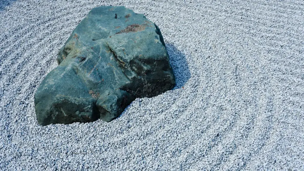 Ein großer grauer Stein ruht inmitten eines sorgfältig geharkten Zen-Gartens aus Kies.