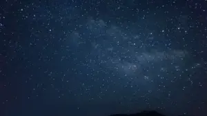 Ein beeindruckender Sternenhimmel über einer ruhigen Berglandschaft in der Nacht.