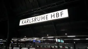 Das beleuchtete Schild des Karlsruher Hauptbahnhofs bei Nacht über den Gleisen.