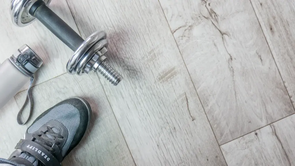 Sportausrüstung mit Hantel, Laufschuh und Wasserflasche auf hellem Holzhintergrund