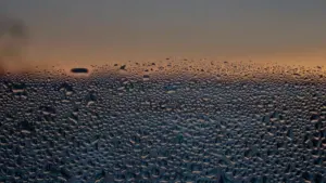 Wassertropfen auf einer Fensterscheibe vor einem stimmungsvollen Sonnenuntergang in Deutschland.